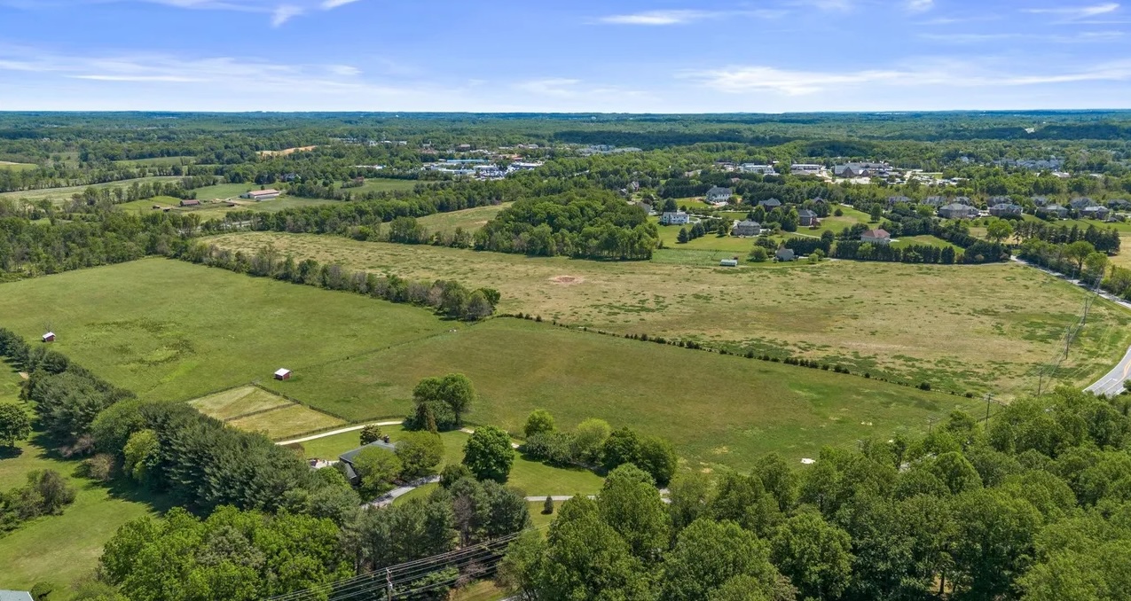 Open fields and mature tree lines across Maysarah Farm in Clarksville, Maryland, seen from above on a clear summer day.